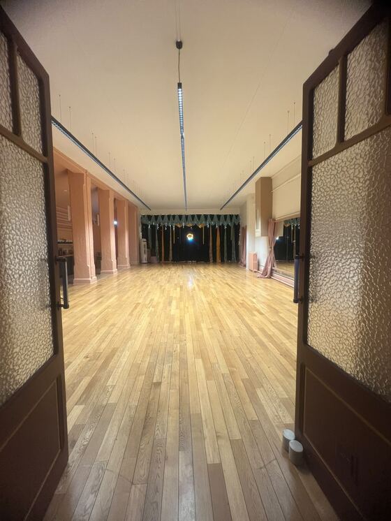 La salle vue depuis ses portes vitrées ouvertes, parquet en chêne clair et scène au fond